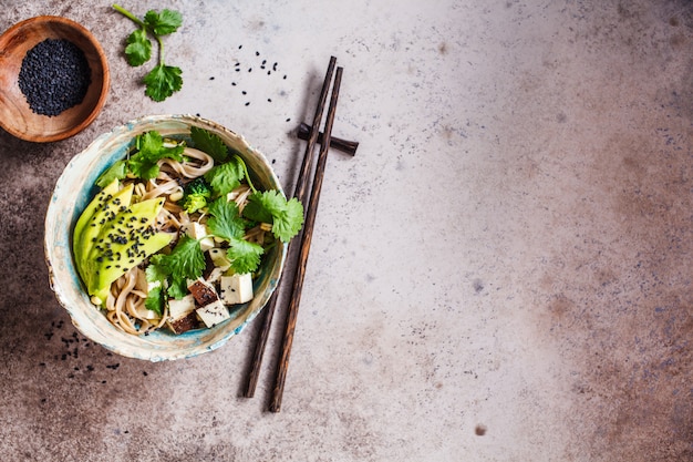 Buckwheat noodles - soba with tofu, broccoli, avocado, seedlings and cilantro, top view, copy space. healthy vegan food concept.