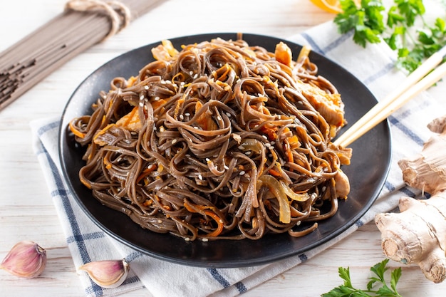 Buckwheat noodles with vegetables and meat decorated with sesame in bowl on a table