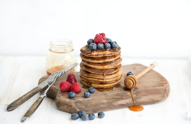 Frittelle di grano saraceno con frutti di bosco freschi e miele su tavola di legno rustica