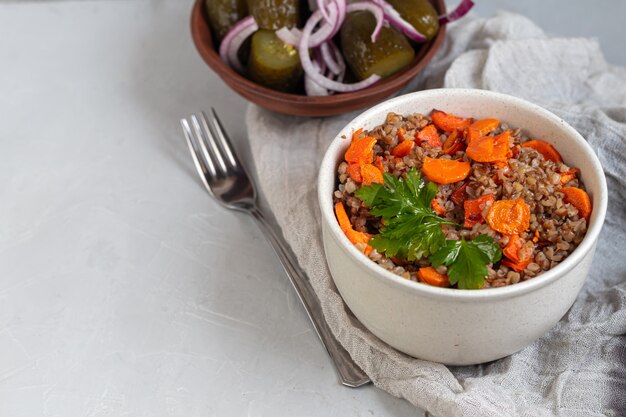 Buckwheat porridge in a bowl with stewed carrots. Decorated with green leaves.