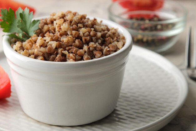 Buckwheat. Porridge cereals with parsley in a white ceramic bowl and tomato on a bright table. breakfast, healthy food.