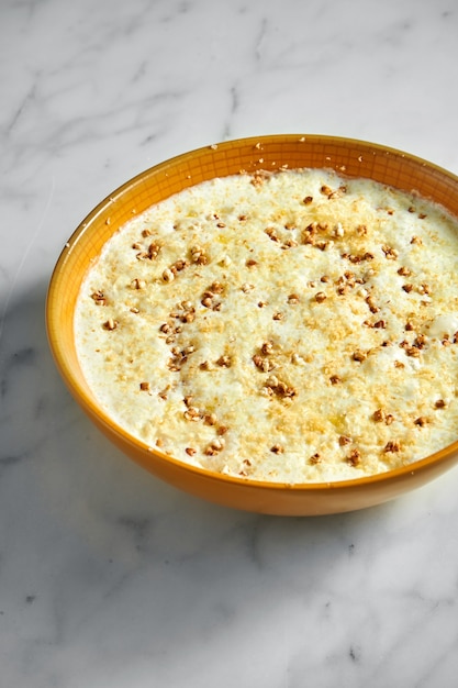 Buckwheat porridge cooked on milk in a bright yellow bowl on light marble