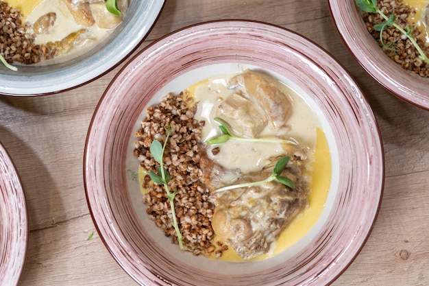 Buckwheat porridge with a chicken on a white plate On a wooden table with gravy and herbs Top view