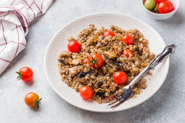 Porridge di grano saraceno con funghi e pomodorini su un piatto.