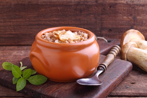 Buckwheat porridge with white mushrooms in a clay bowl on a wooden background