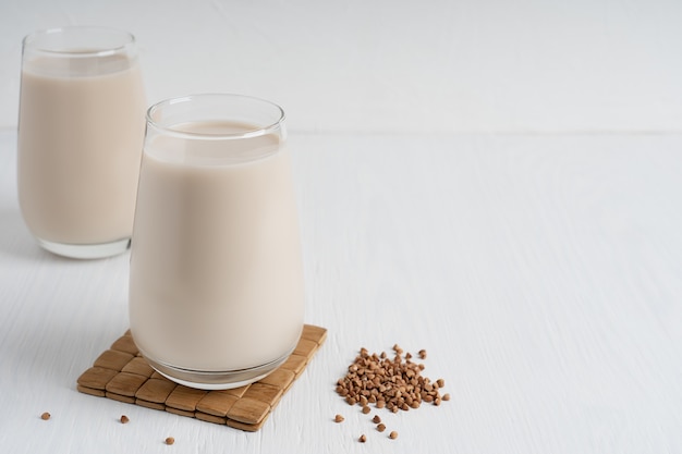 Buckwheat seeds and glass of lactose free vegetarian milk on white wooden table