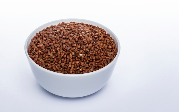 Buckwheat seeds isolated on white, ceramic bowl full of buckwheat grains