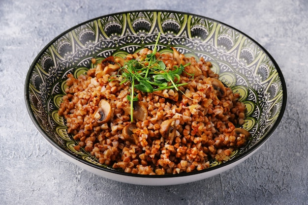 Buckwheat with mushrooms and microgreens of peas on concrete table.