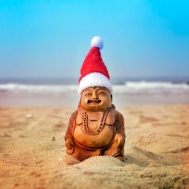 Фото Статуэтка будды в рождественской шапке на пляже волны на заднем плане