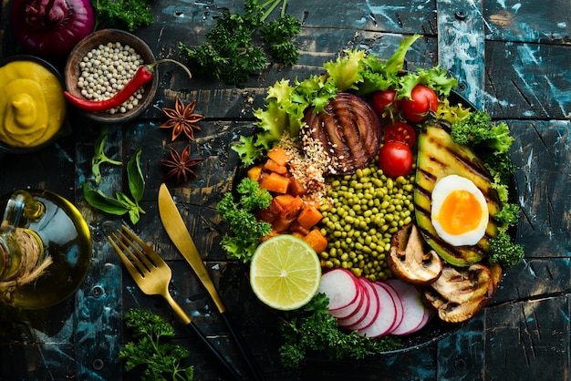 Photo buddha bowl avocado mung bean pumpkin mushrooms tomatoes and lettuce in a black bowl vegan diet top view free space for text