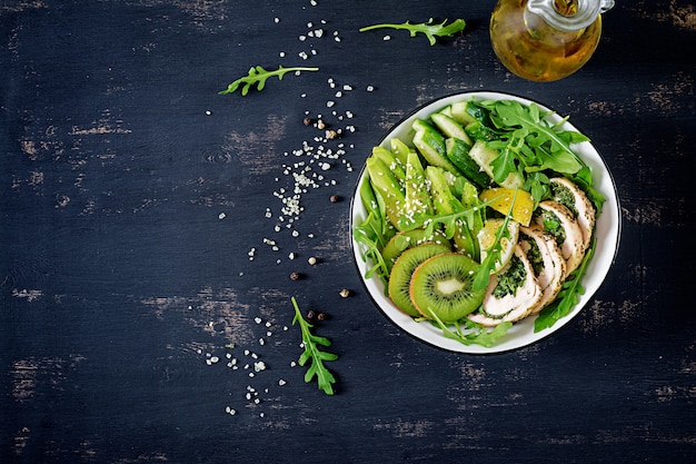 Buddha bowl dish with chicken fillet, avocado, cucumber, fresh arugula salad and sesame. detox and healthy keto diet bowl concept. overhead, top view, flat lay, copy space