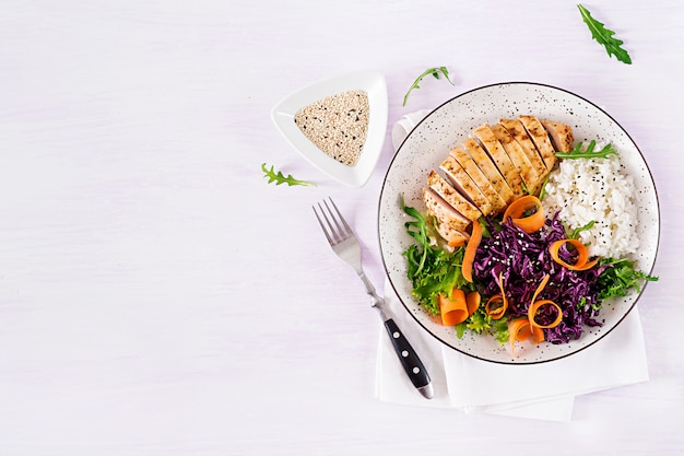 Photo buddha bowl dish with chicken fillet, rice, red cabbage, carrot, fresh lettuce salad and sesame.