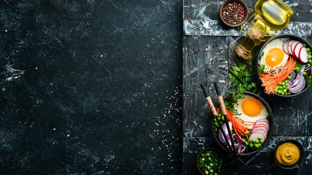 Buddha bowl egg green peas onion radish and carrots in a black stone bowl