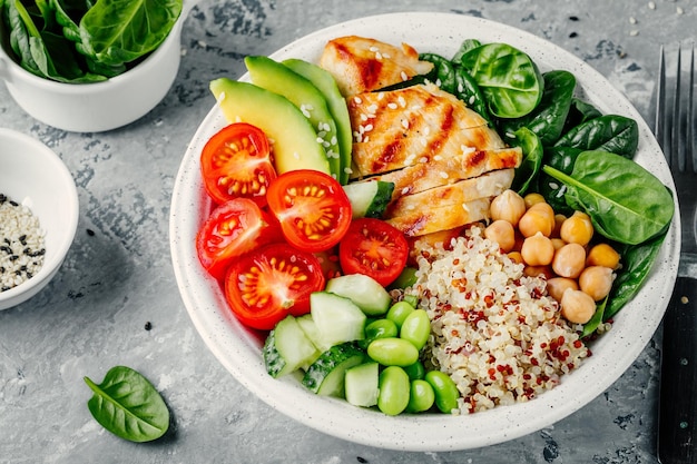 Buddha bowl met spinaziesalade quinoa geroosterde kikkererwten gegrilde kip avocado tomaten komkommers sesamzaadjes