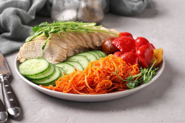 Photo buddha bowl with baked chicken, fresh cucumber, peas microgrines, carrots and sweet pepper on a gray concrete background.