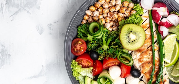 Buddha bowl with kale salad, avocado, asparagus, chickpeas, broccoli, radish, chicken, cucumber, tomatoes, olives and mozzarella. Long banner format, top view