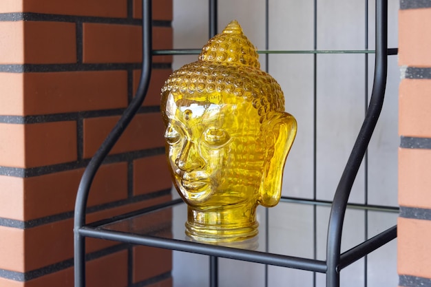Buddha head made from transparent yellow glass on the shelf decoration element in oriental style