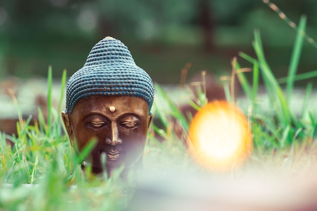 Buddha's head Sculpture in the grass with candlelight in the foreground