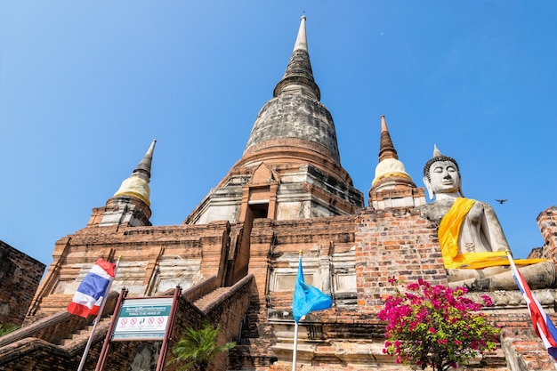 Photo buddha statue at the bottom of a large ancient pagoda on blue sky background at wat yai chai mongkon temple in phra nakhon si ayutthaya historical park, ayutthaya province, thailand