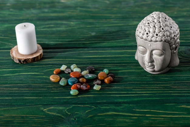 Buddha statuette candle and colorful semiprecious stones on wooden surface