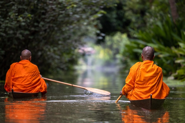 buddhist monk in small wooden boat sailing in canal for receive food in morning