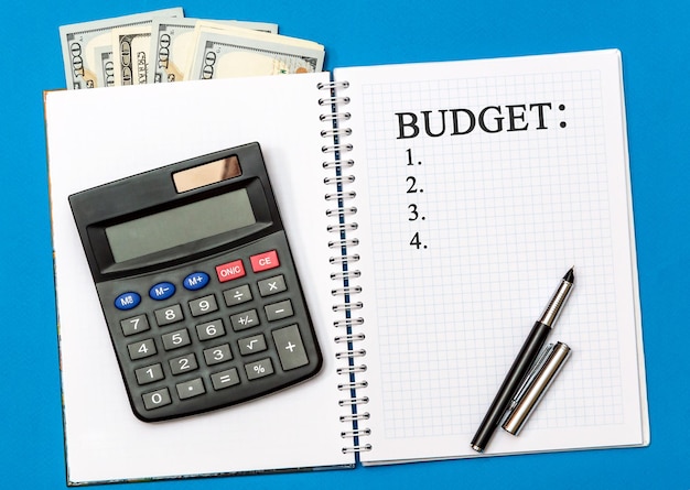 Список бюджета в блокноте с деньгами и калькулятором на синем Концепция планирования бюджета Вид сверху