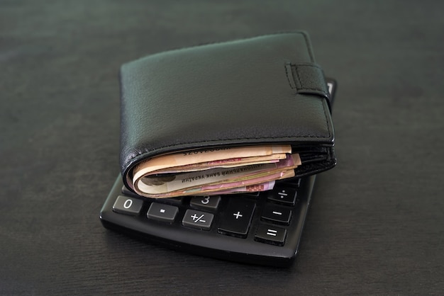 予算とお金の概念。黒いテーブルに電卓が付いたお金でいっぱいの財布。