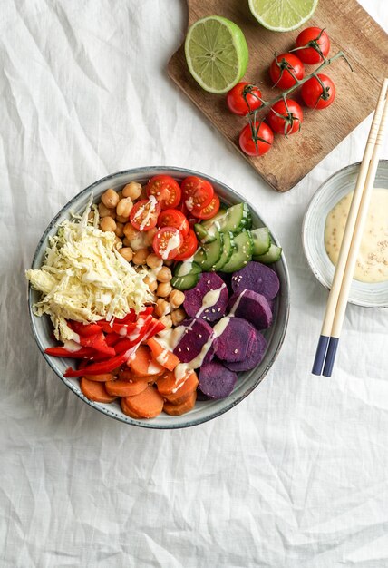 Budha kom met paarse batata, paprika, kool, zoete aardappelen, kikkererwten, komkommers op het witte linnen tafelkleed