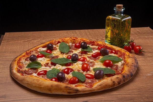 Buffelmozzarellapizza met gesneden pepperonis, cherrytomaatjes, zwarte olijven en basilicum op tafel