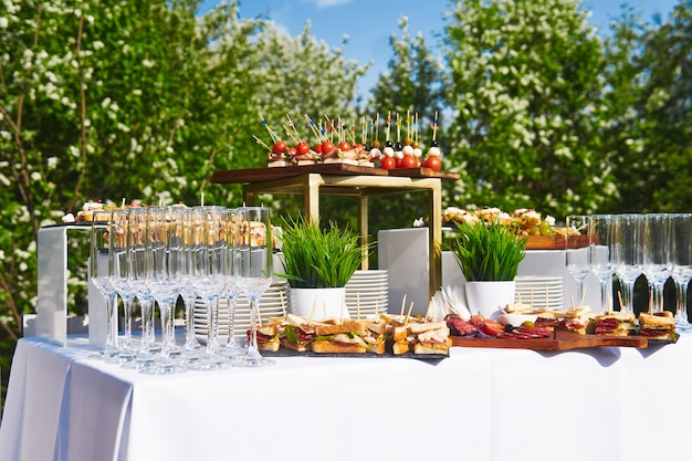 Buffet in de open lucht - een tafel met hapjes en glazen tegen de achtergrond van bloeiende bomen en de lucht