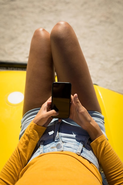 Buik van blanke vrouw liggend op een strandbuggy aan zee met behulp van smartphone. strandvakantie tijdens een roadtrip in de zomervakantie.