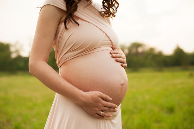 Buik van een zwangere vrouw bij zonsondergang. Zwanger meisje dat de baby voelt