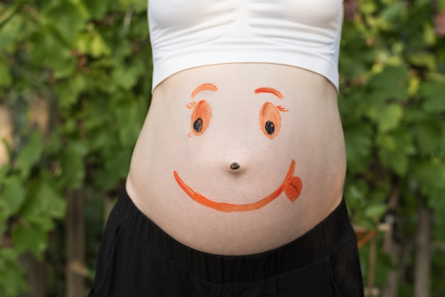 Buik van een zwangere vrouw met een geverfd lachend gezicht.