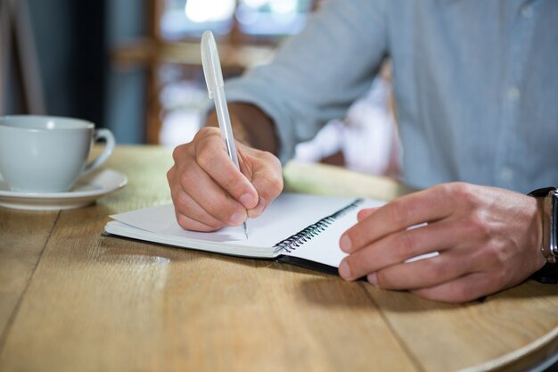 Buik van jonge man schrijven in dagboek aan tafel in coffeeshop