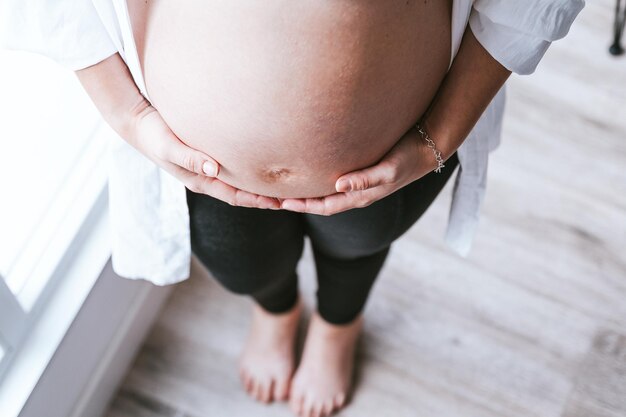 Buik van onherkenbare zwangere vrouw die haar buik met beide handen vasthoudt