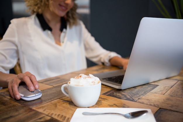 Buik van vrouw met laptop met koffie op tafel in café