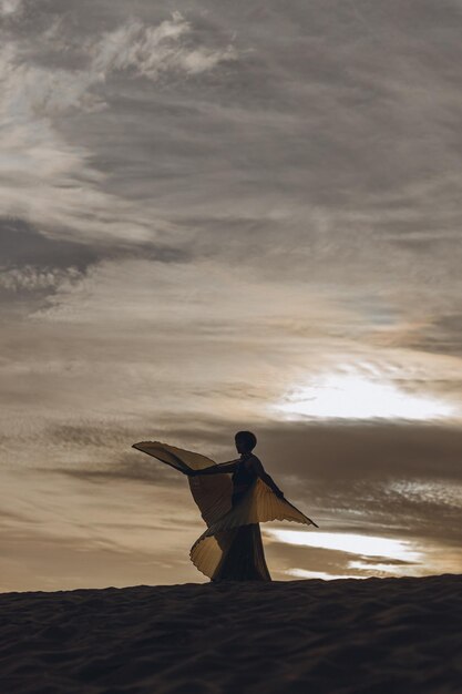 Foto buikdanser die met gouden vleugels op het zand danst.