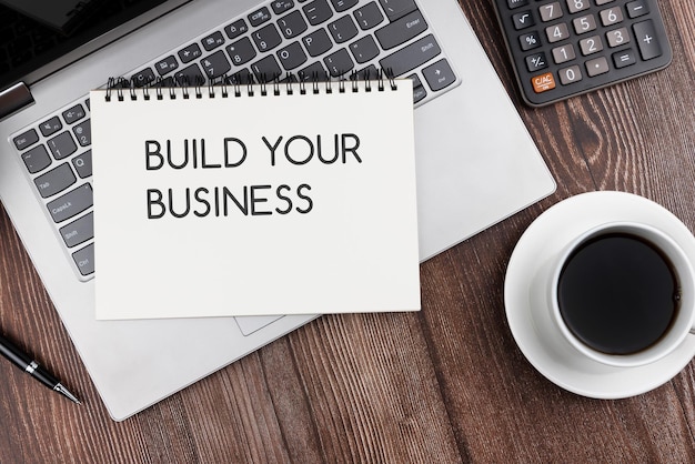 Build your business text on note pad with laptop and cup of black coffee flat lay