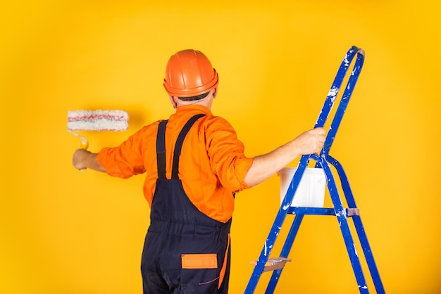 自分で未来を築くアパートで働く職人ペイントローラー塗装とリフォームビジネスで修理ツールを作る建設現場で働く画家シニアマンははしごでローラーを使用する