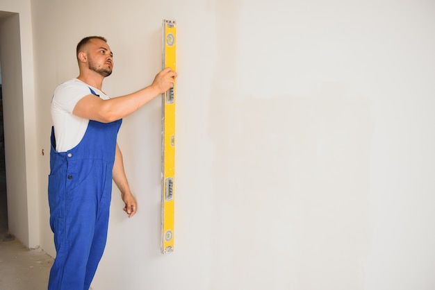 The builder carefully corrects the irregularities of the wall with a trowel. Builder in work clothes against a gray wall. Photo plasterer at work.