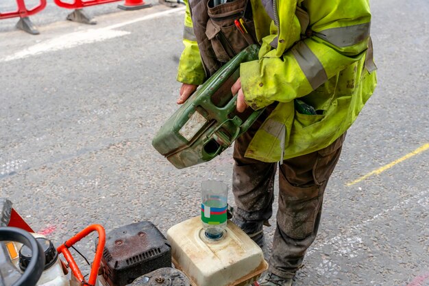 Builder filling petrol powered road saw fuel tank with petrol before cutting asphalte road surface