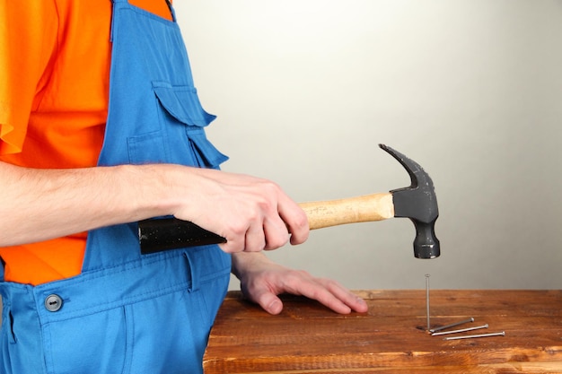 Builder hammering nails into board on grey background