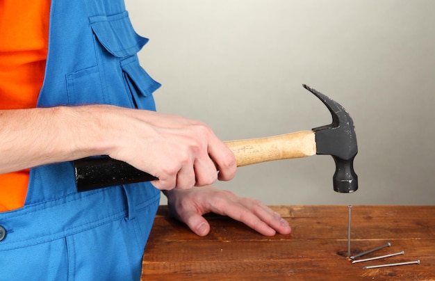 Photo builder hammering nails into board on grey background