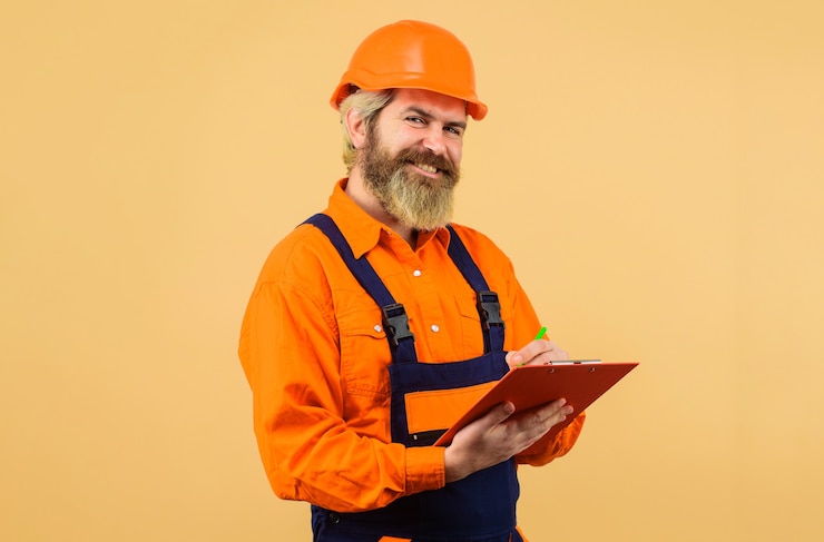  Builder in hard hat and overalls making notes in clipboard. construction worker or repairman with f