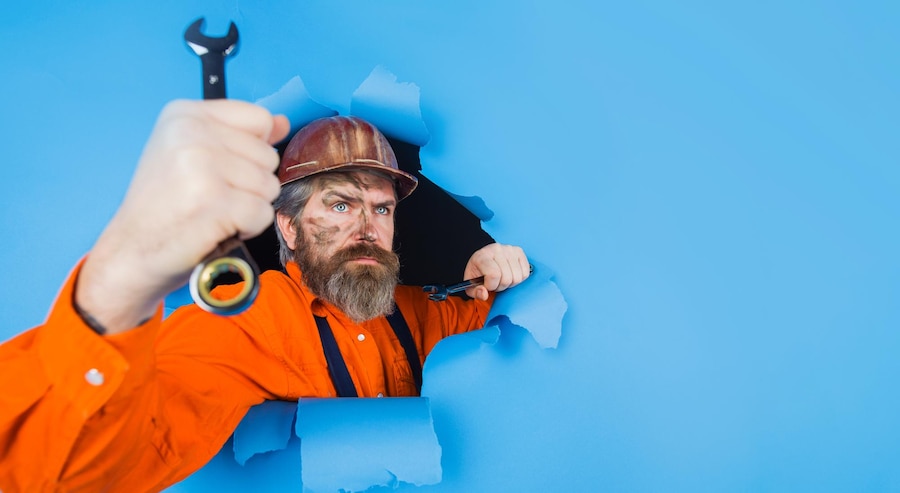  Builder in hardhat with wrench looking through paper hole bearded man with spanner selective focus