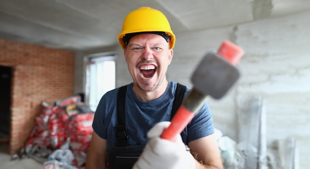 Builder in helmet holds sledgehammer hammer and screams