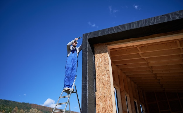 builder installing corrugated iron sheet used as facade of future wooden frame house