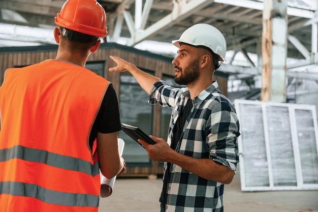 Builder is talking with manager or architect Two workers are in the industrial wooden warehouse