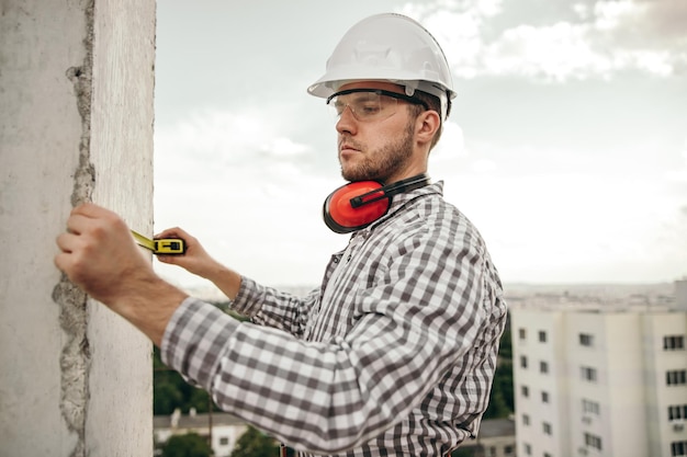 Builder measuring wall on construction site