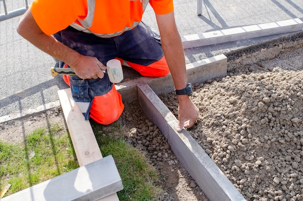 Builder  placing edging pin kerb into semidry concrete using a string line to keep them straight